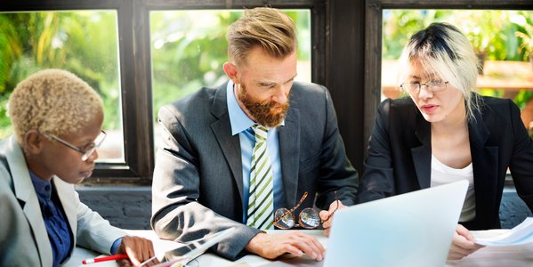 Three people gather around a laptop.
